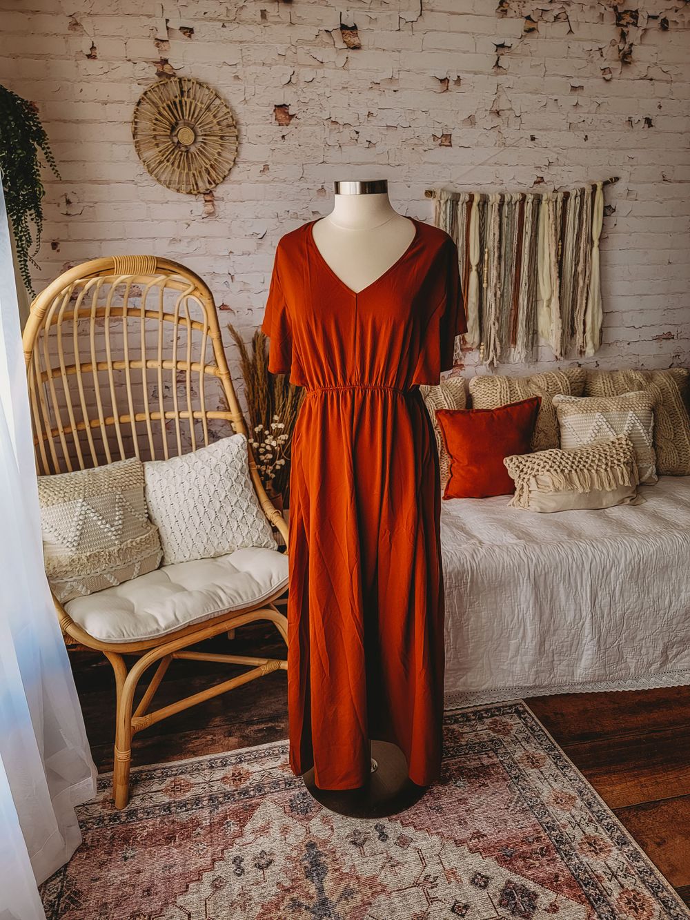 Burnt orange V-neck midi dress with elbow sleeves and elastic waist on a mannequin in a boho styled room.
