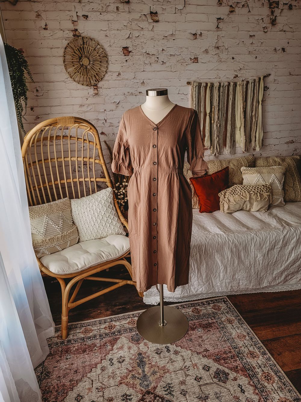 Taupe button-front midi dress with puff sleeves and V-neckline on a mannequin in a boho styled room.