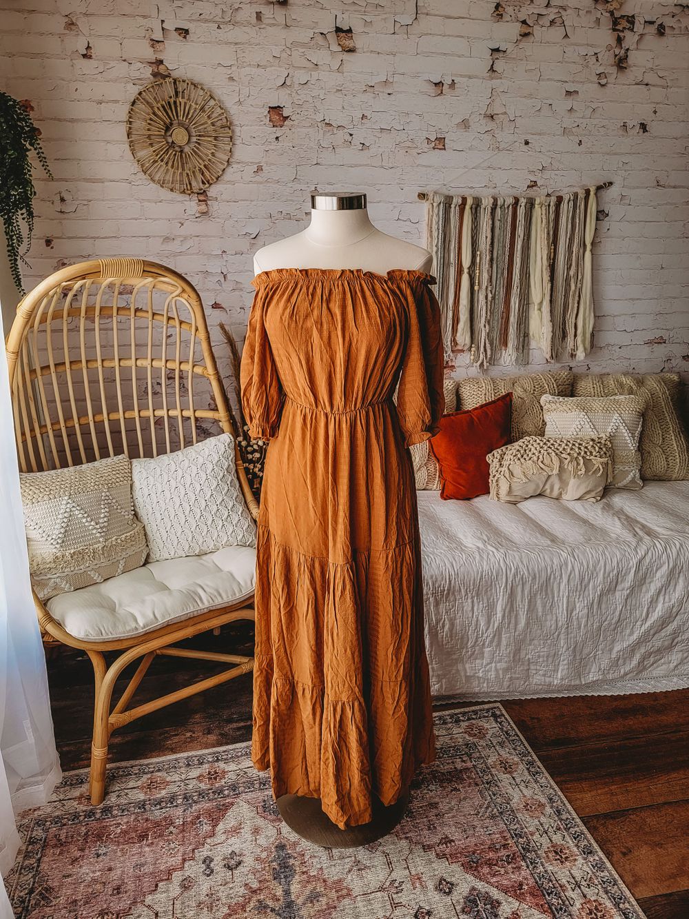 Rust orange off-shoulder tiered maxi dress on mannequin in bohemian styled room.