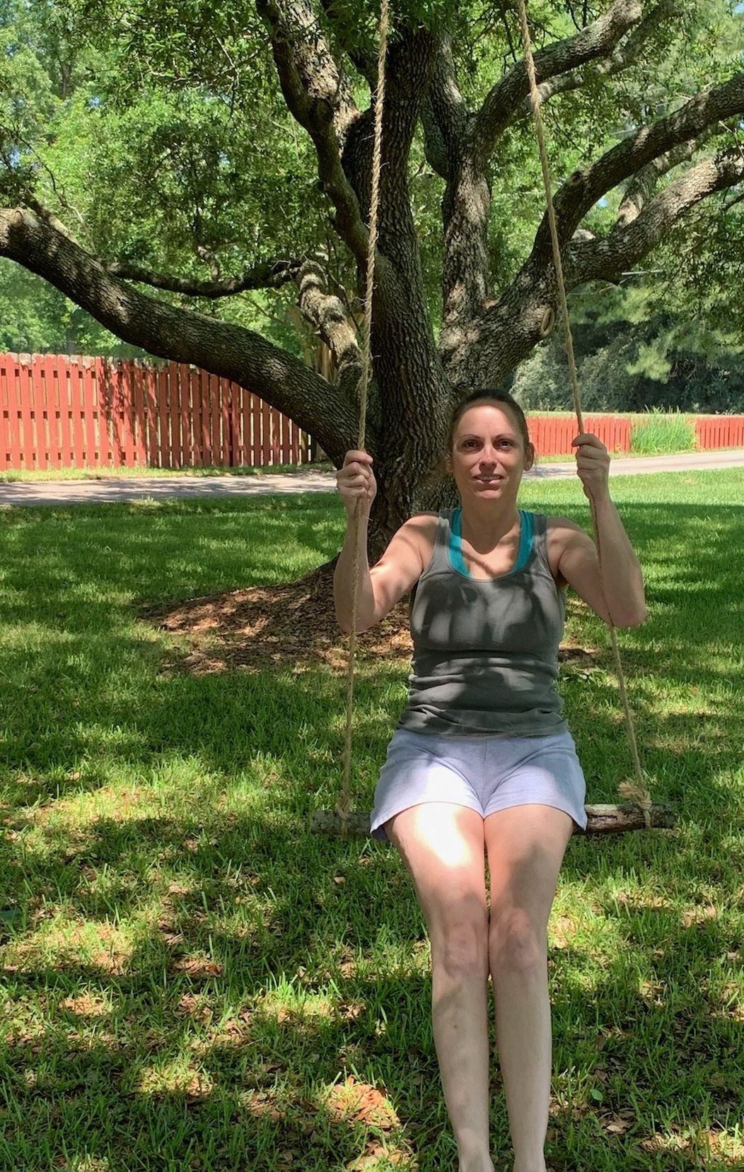 Woman enjoying rope swing under large shady tree in backyard.