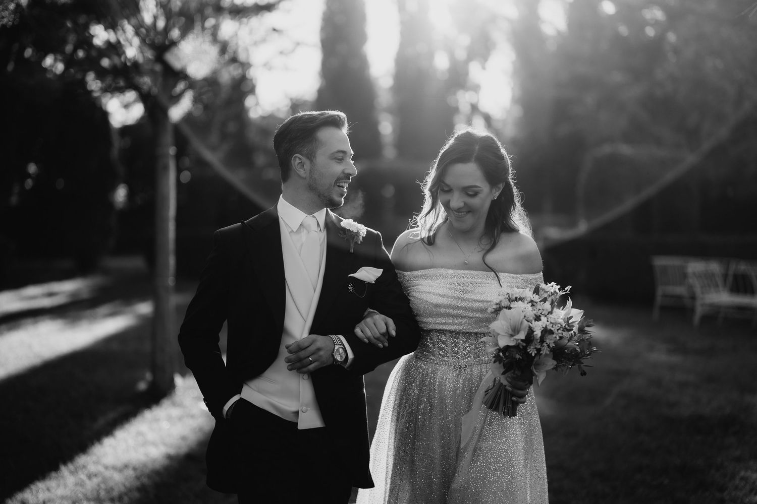 A joyful wedding couple walking together in sunlit garden.