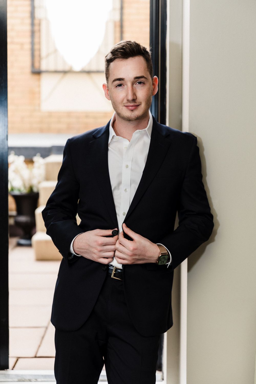 Business portrait of man in black suit standing by window.