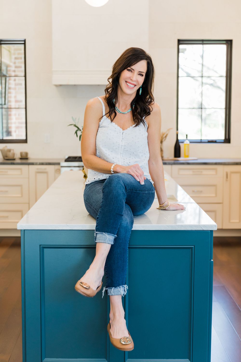 Casual portrait of woman sitting on blue kitchen island in modern home.