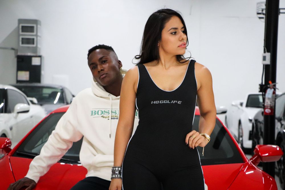 Models in casual attire pose next to luxury vehicles in a white showroom.