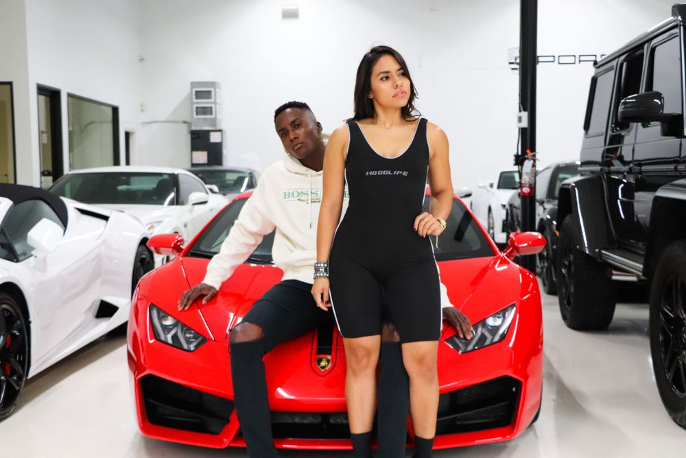 Models posing against a bright red Lamborghini in an upscale car showroom.