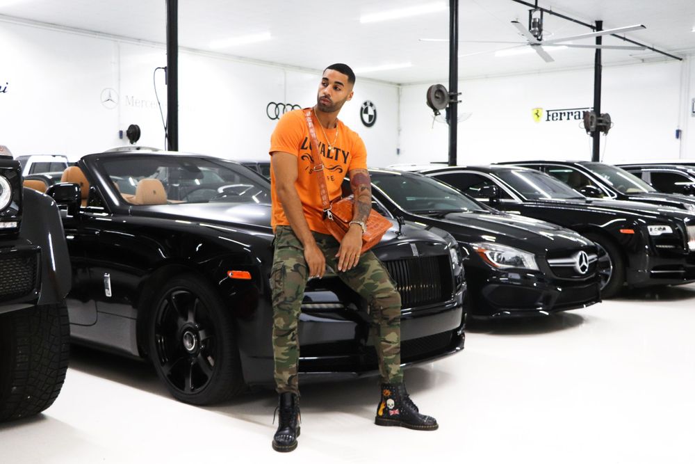 Orange-clad model sits on black Rolls Royce in luxury car dealership.