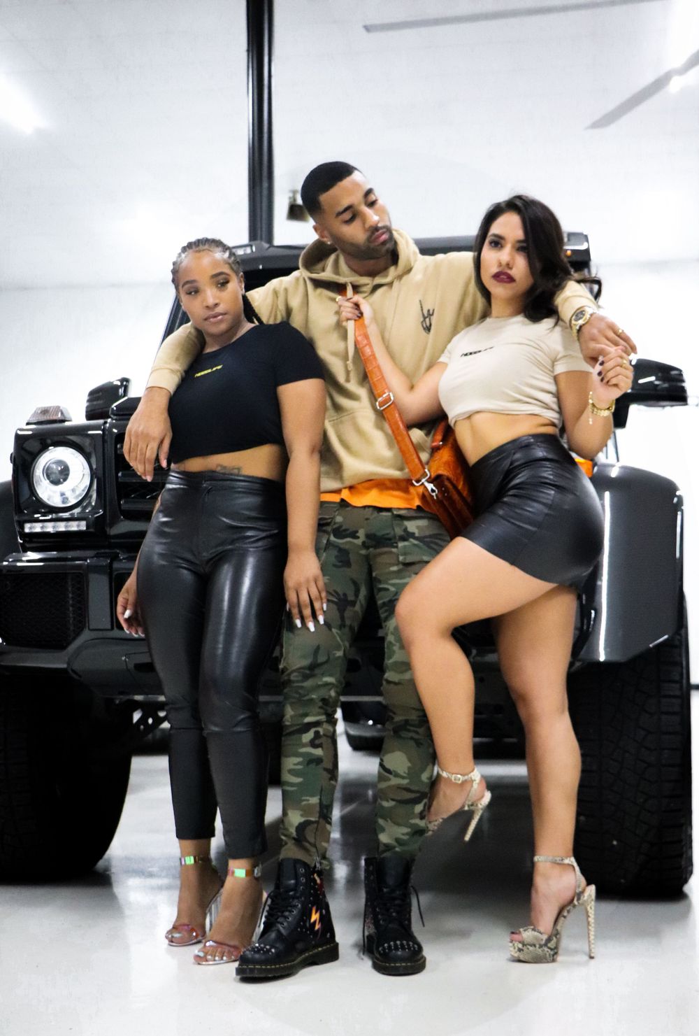 Fashion models pose against black luxury SUV in modern showroom setting.