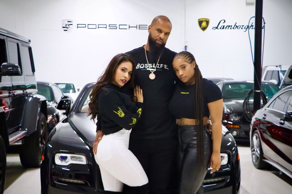 Lifestyle photoshoot in luxury car showroom with Porsche and Lamborghini logos.