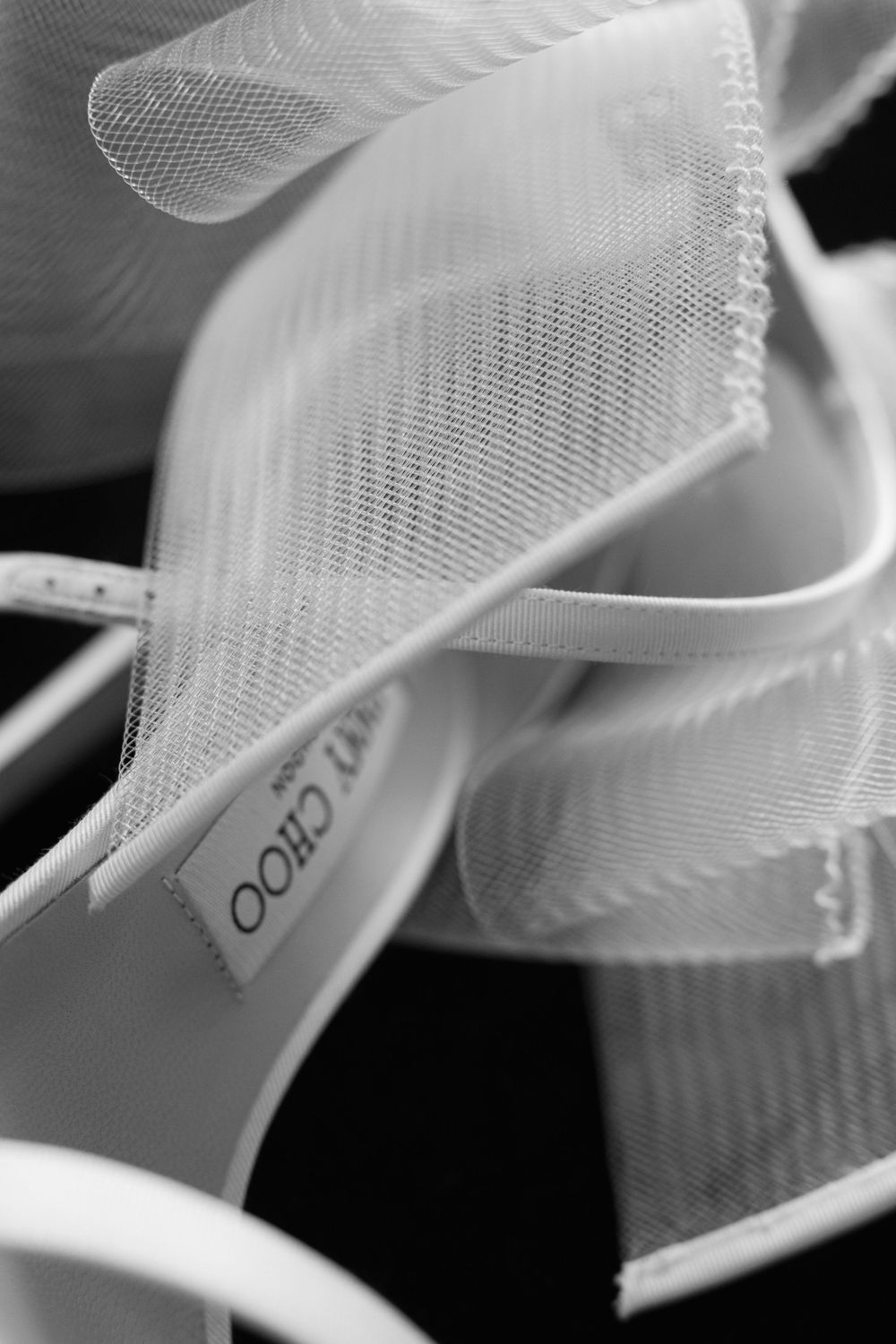 Close-up detail of sheer white tulle fabric and a Jimmy Choo wedding shoe label in black and white.