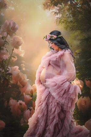 Dreamy outdoor maternity portrait with flowing pink ruffled dress in garden setting.