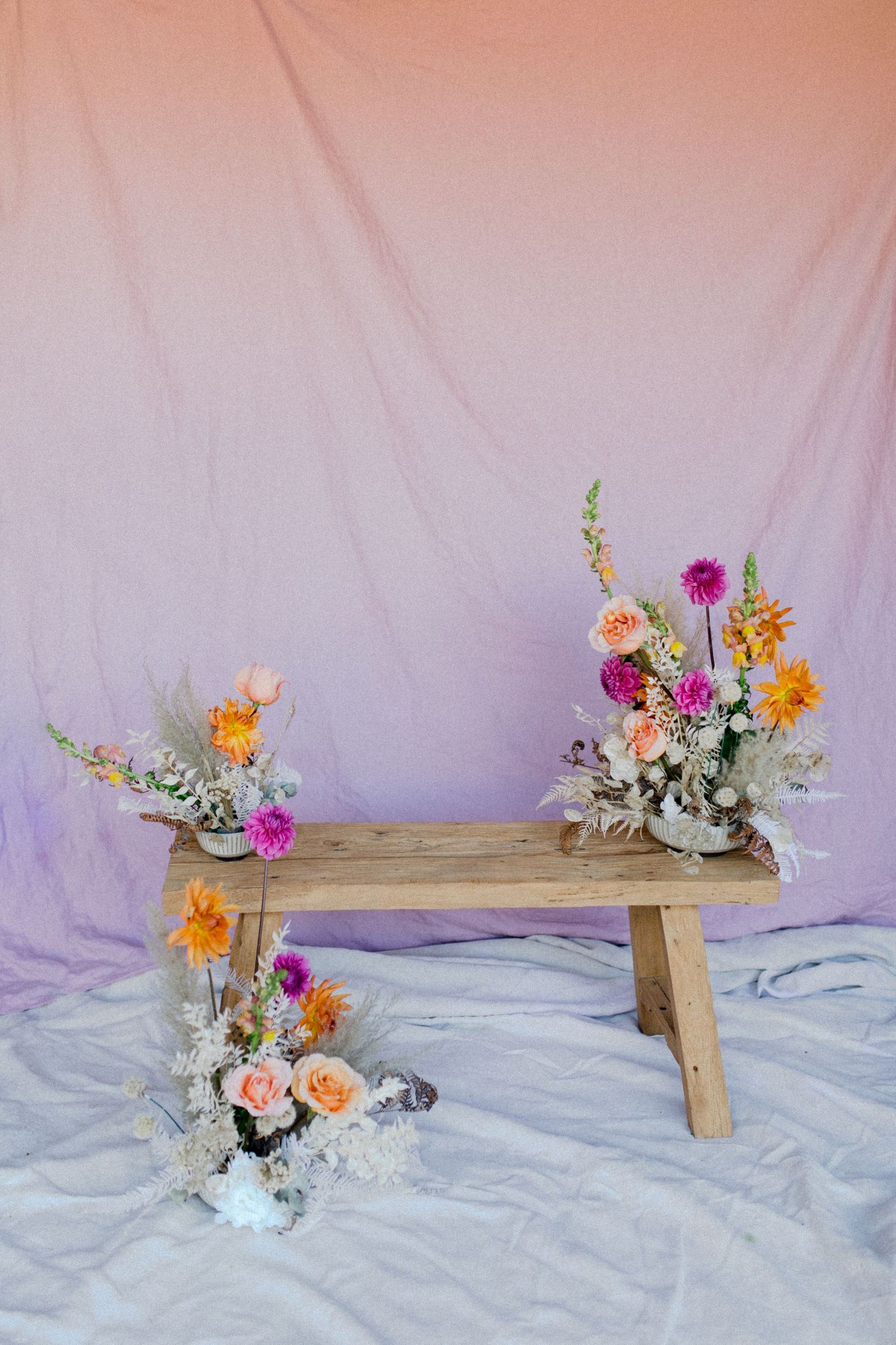 Rustic wooden bench adorned with pink, orange and purple flower arrangements.