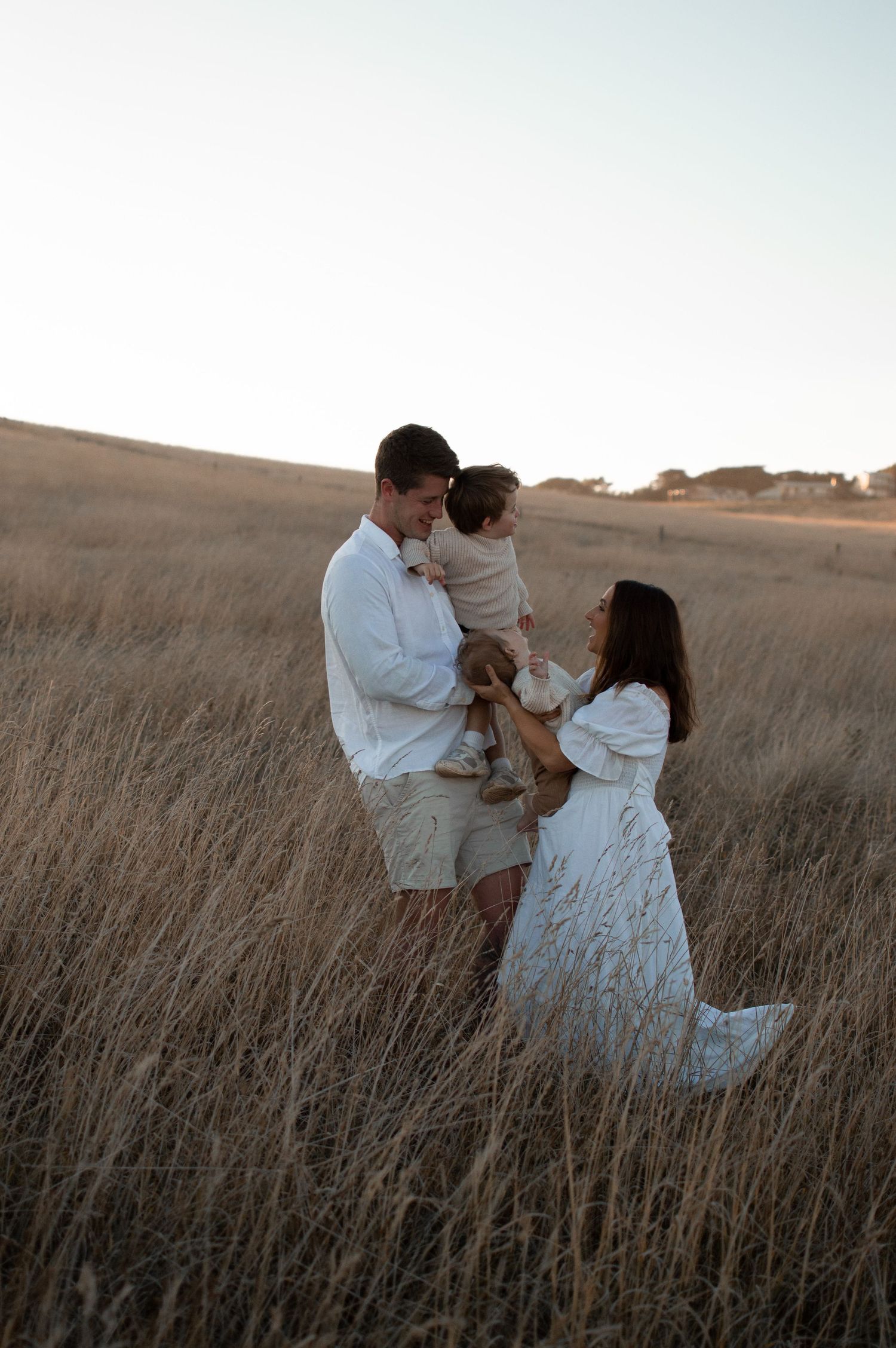 A family shares a tender moment together in a golden field of tall grass during sunset.