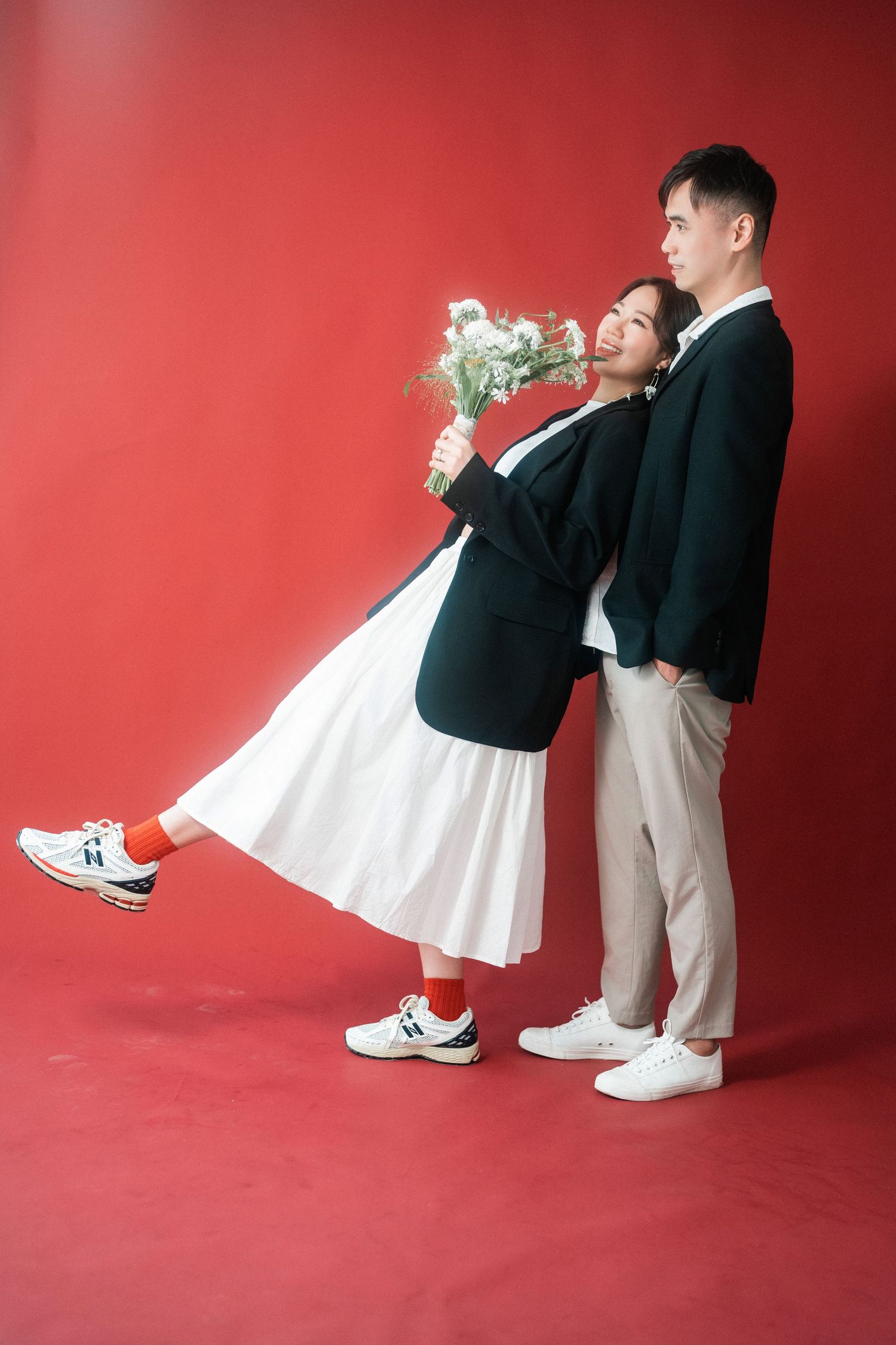 Stylish couple in black and white attire posing against vibrant red backdrop.