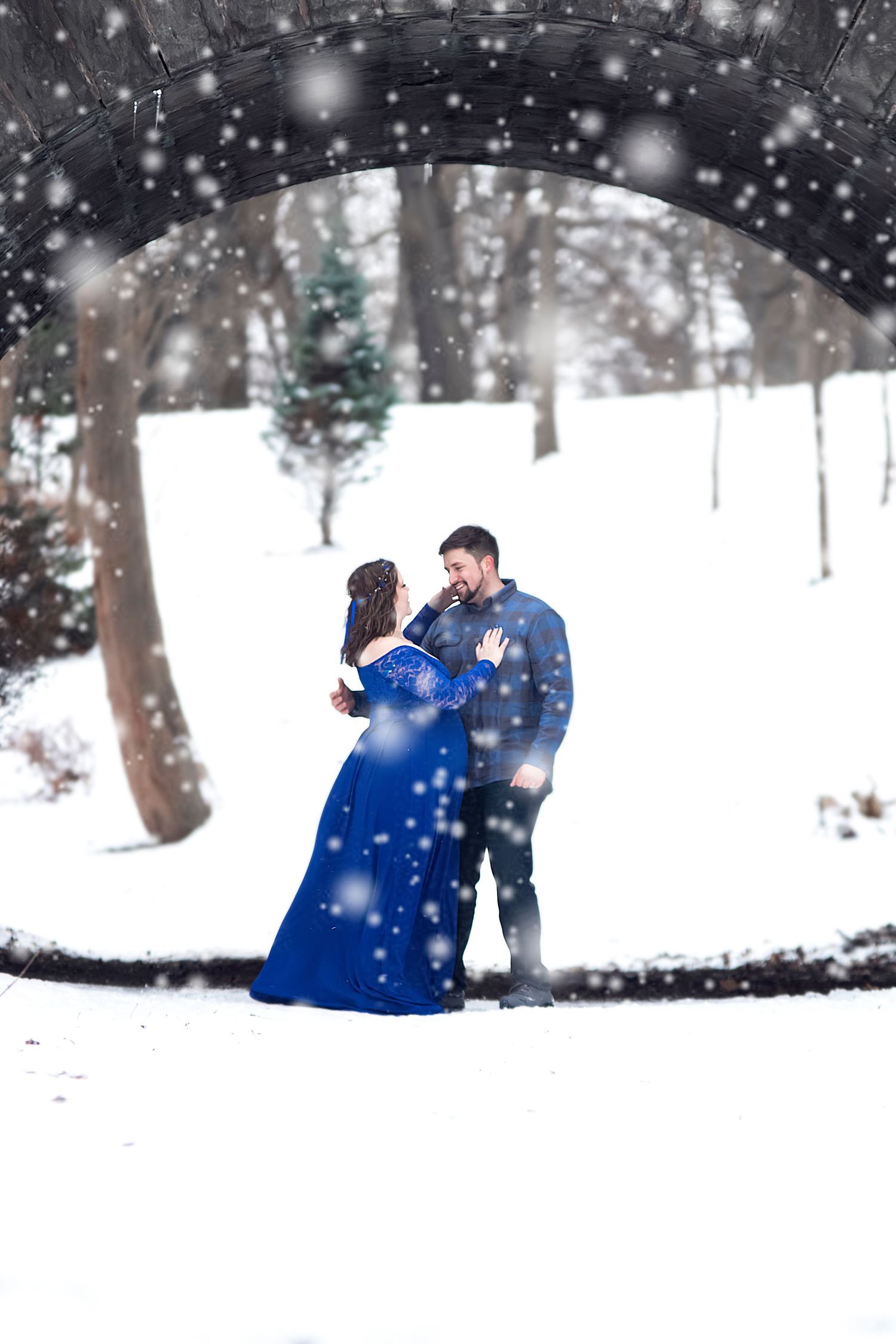 Winter engagement photos in a snowy forest with falling snowflakes and twinkling lights.