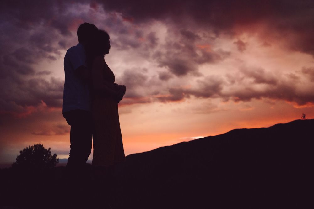 Silhouette of a couple embracing against a dramatic sunset sky with colorful clouds.