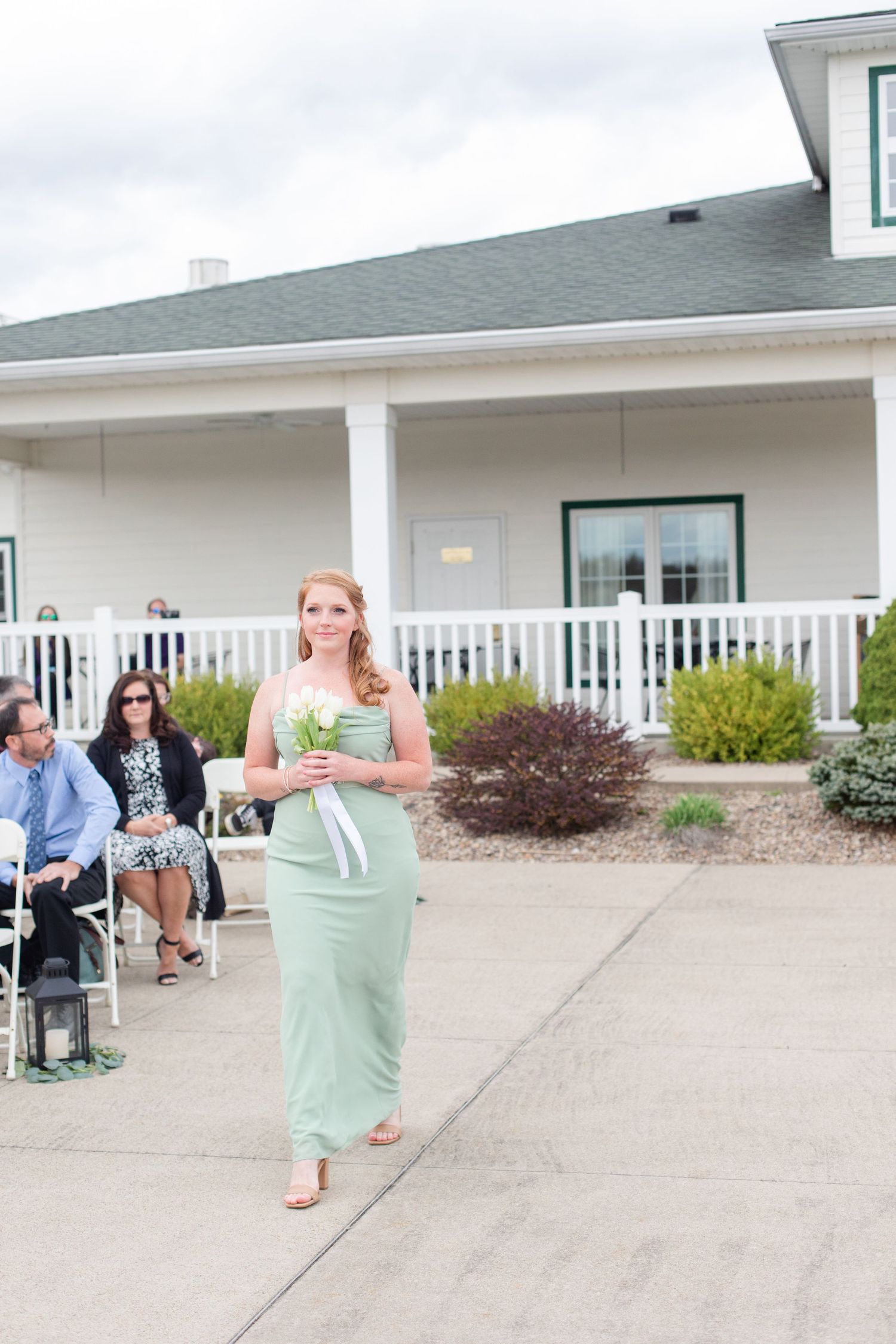A bridesmaid in mint green dress walks down the outdoor aisle at a wedding ceremony.