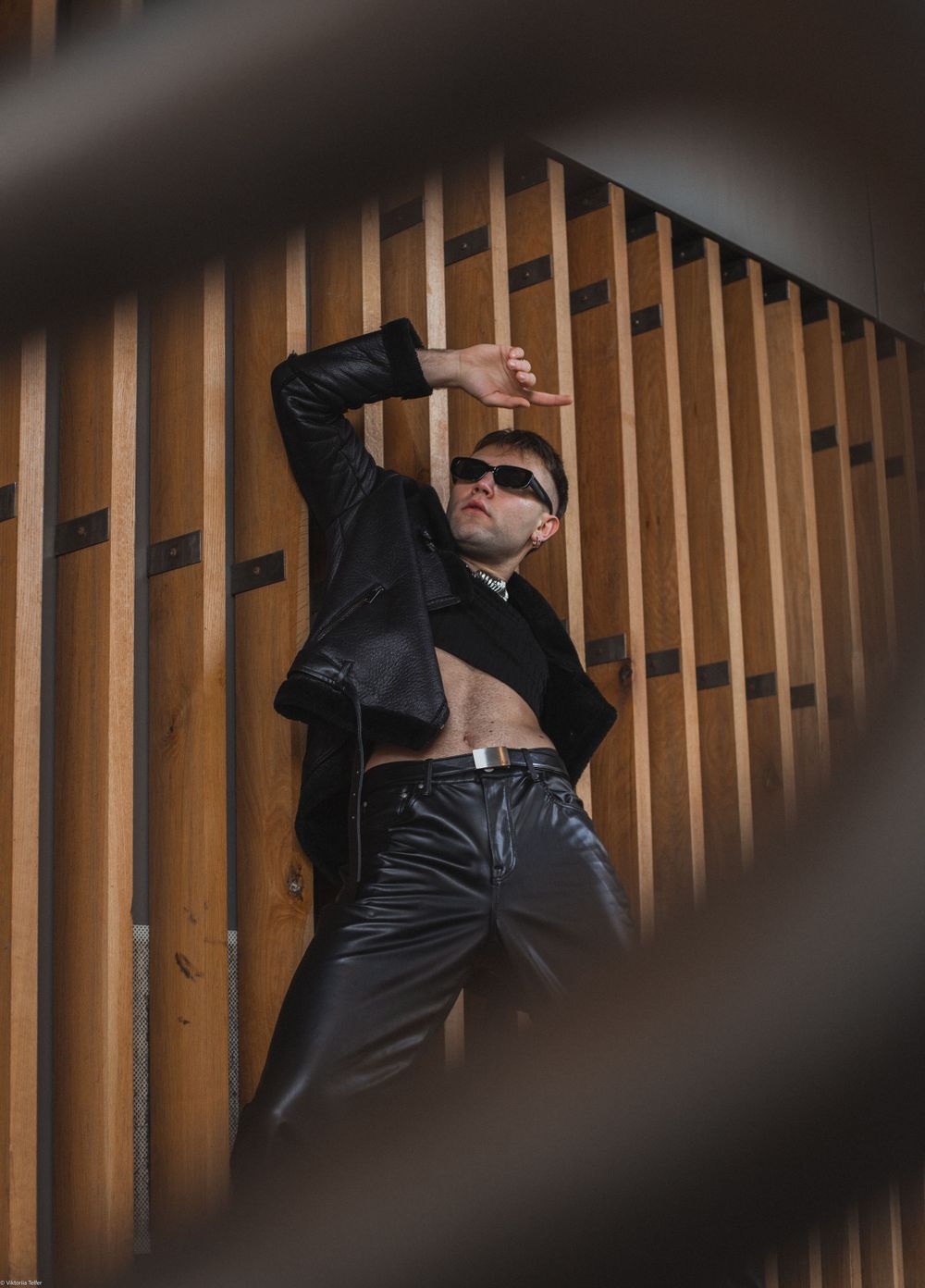 Dramatic fashion pose against wooden slat wall through partial frame view.