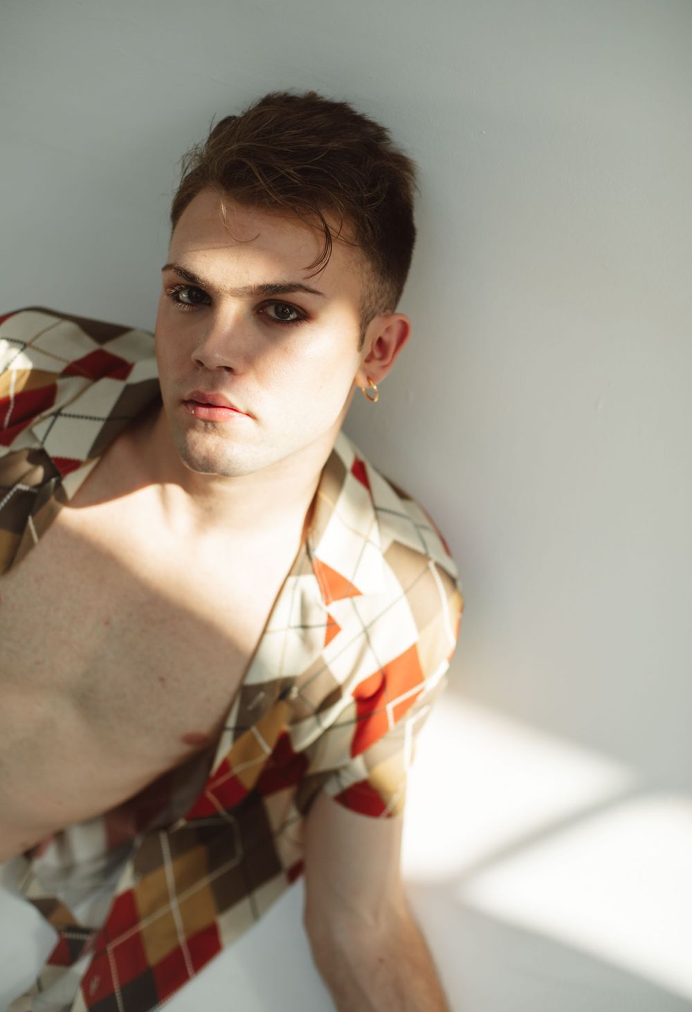 Portrait in geometric patterned shirt with dramatic lighting against light background.