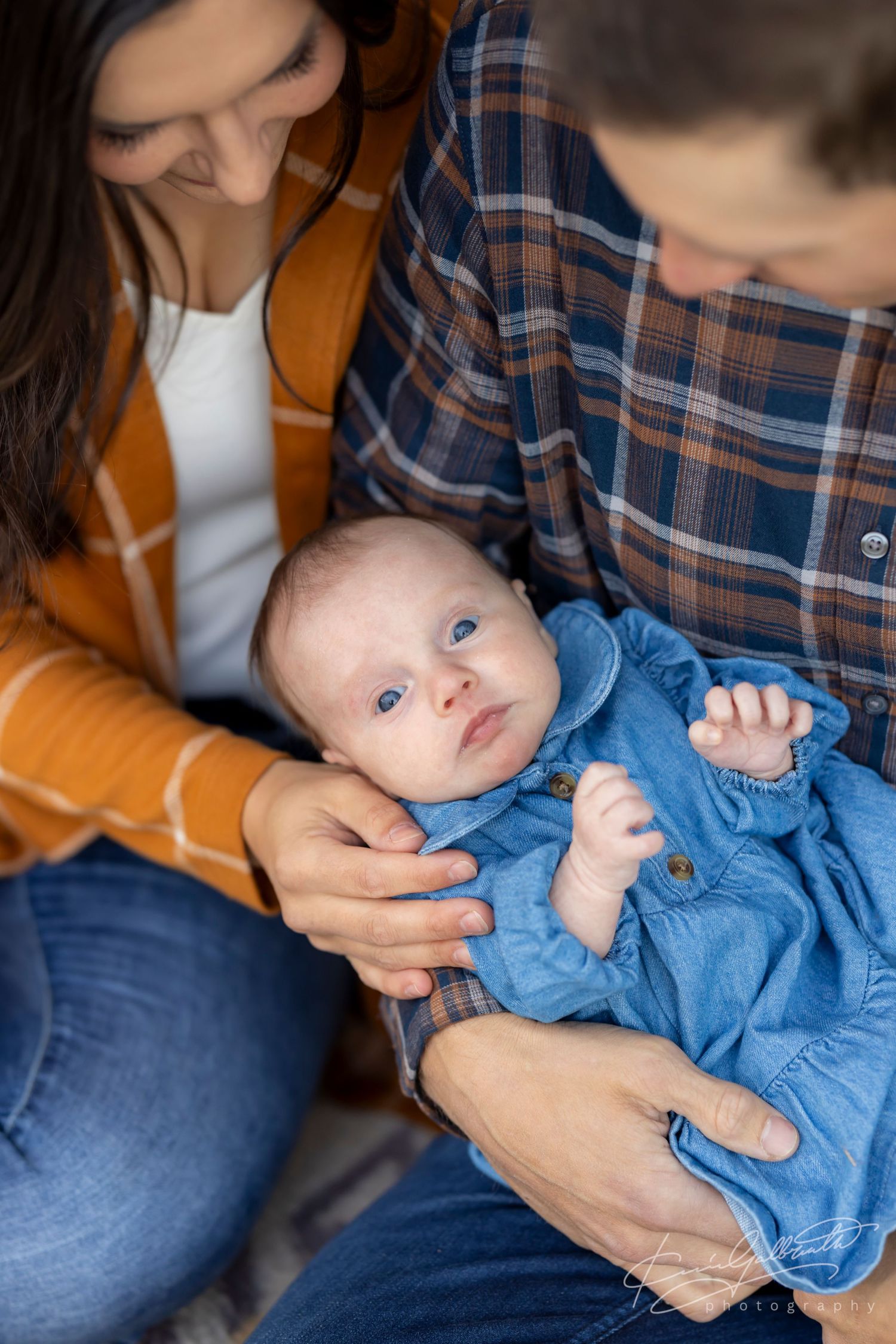 A man and a woman looking down to a baby who is looking up. A baby is swaddled in blue.