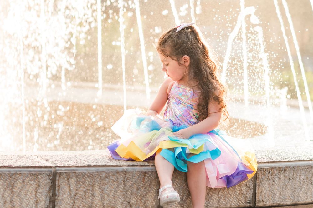 little girl sits in front of fountain in Central Park in Winter Haven, Florida