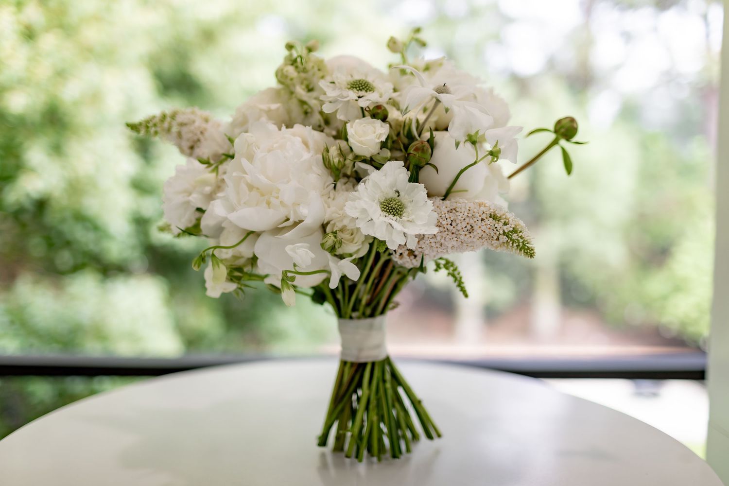 Classic white and green bridal bouquet with mixed flowers on a light surface.