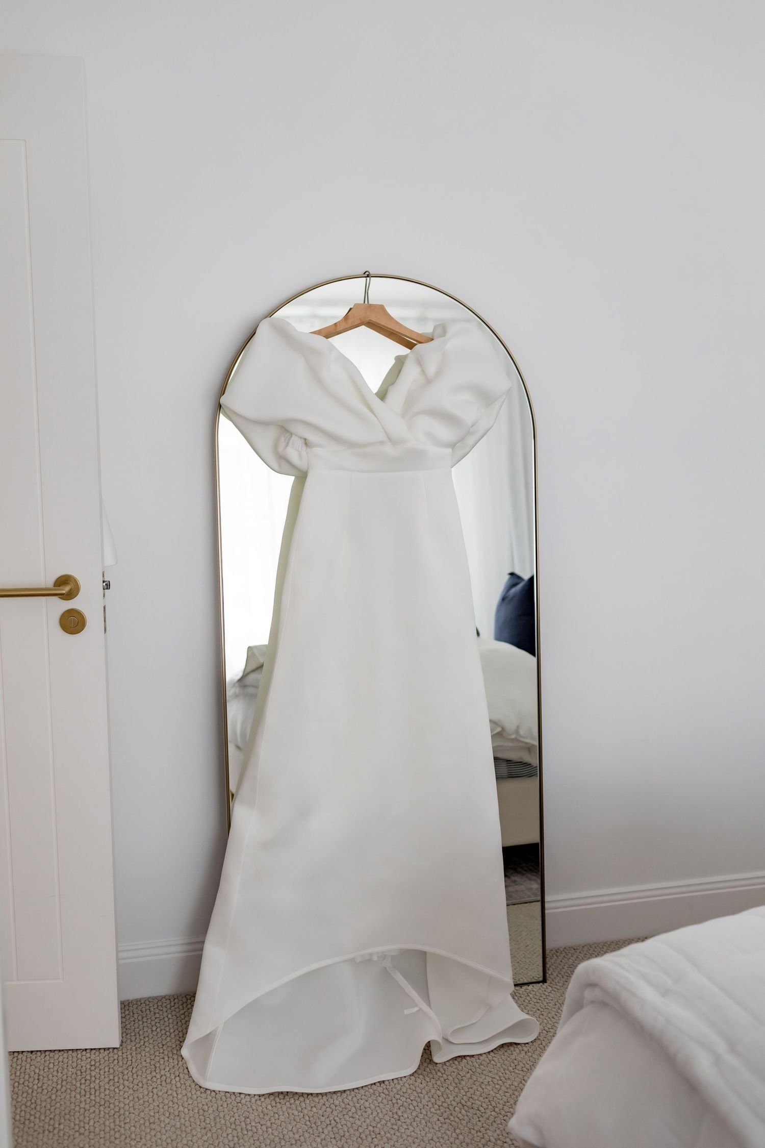 Full-length wedding gown displayed on hanger in front of arched mirror.