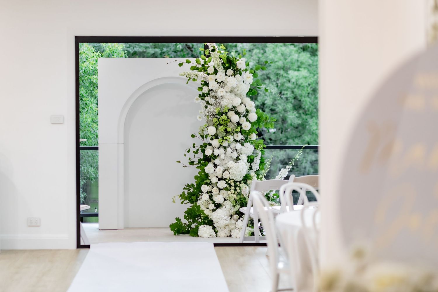 A white floral arch with cascading flowers creates an elegant wedding ceremony backdrop.