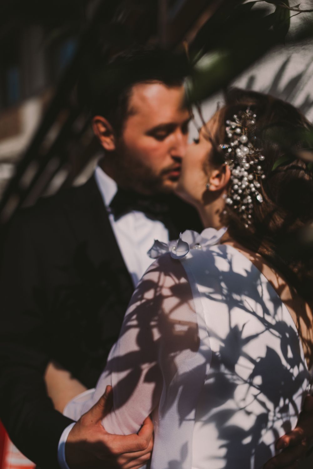 Wedding couple embraces in dramatic lighting with shadows casting artistic patterns.