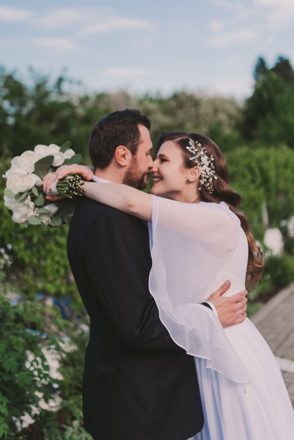Newlyweds share a romantic dance outdoors surrounded by greenery and white flowers.