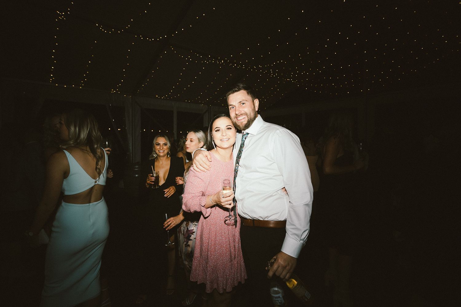 Wedding guests socializing and dancing at a dimly lit indoor reception.
