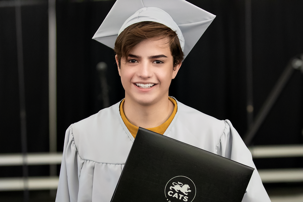 Graduate in white cap and gown holding diploma during commencement ceremony.