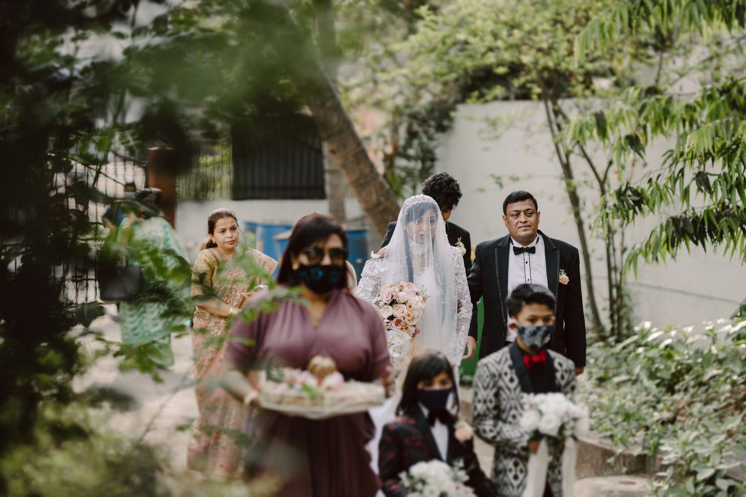 Wedding party members walking through a lush garden path with greenery and flowers.
