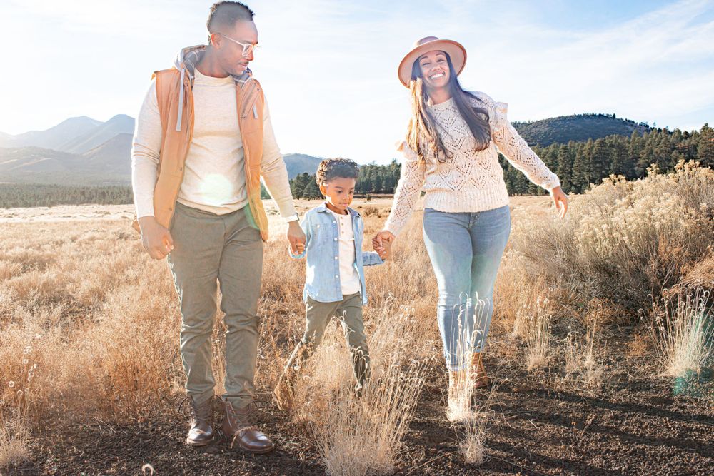 Family jumping together in golden field with mountains in the background at sunset.