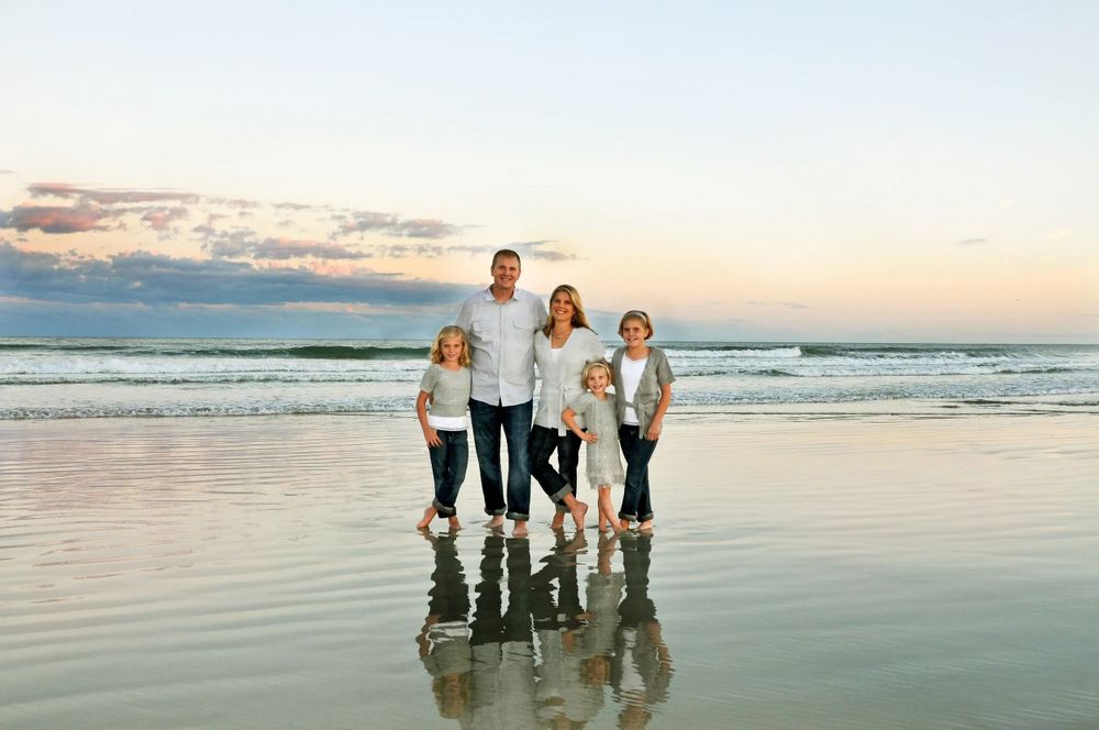 Family standing together on beach at sunset with reflections in wet sand.