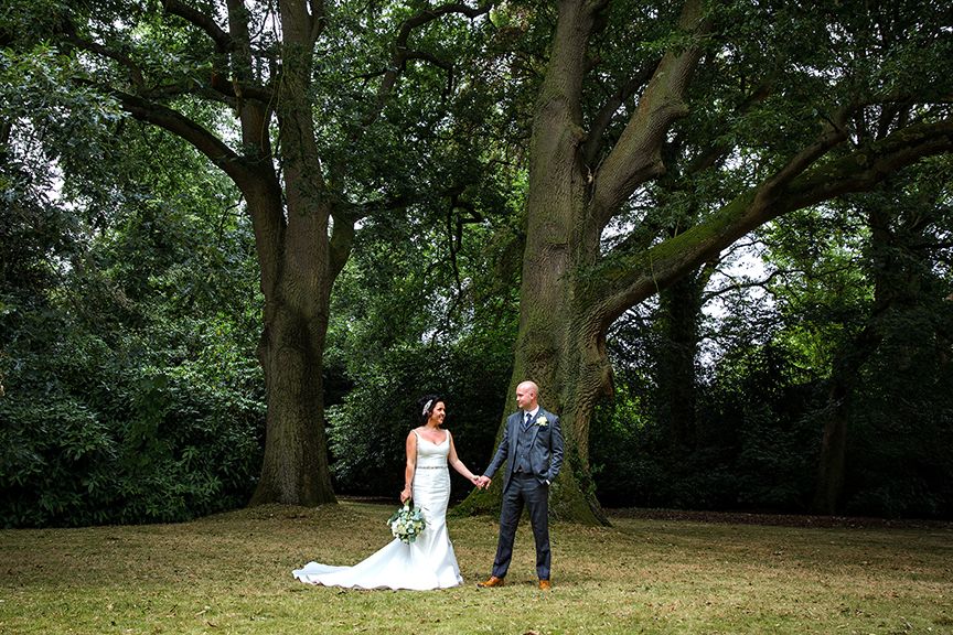 Bride & Groom holding hands beneath a tree at Hampton Manor wedding venue