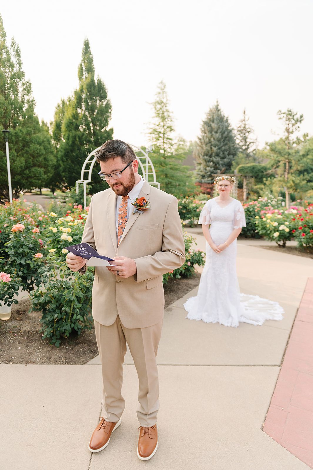 A first look moment before a garden wedding ceremony with a beige suited figure reading notes.