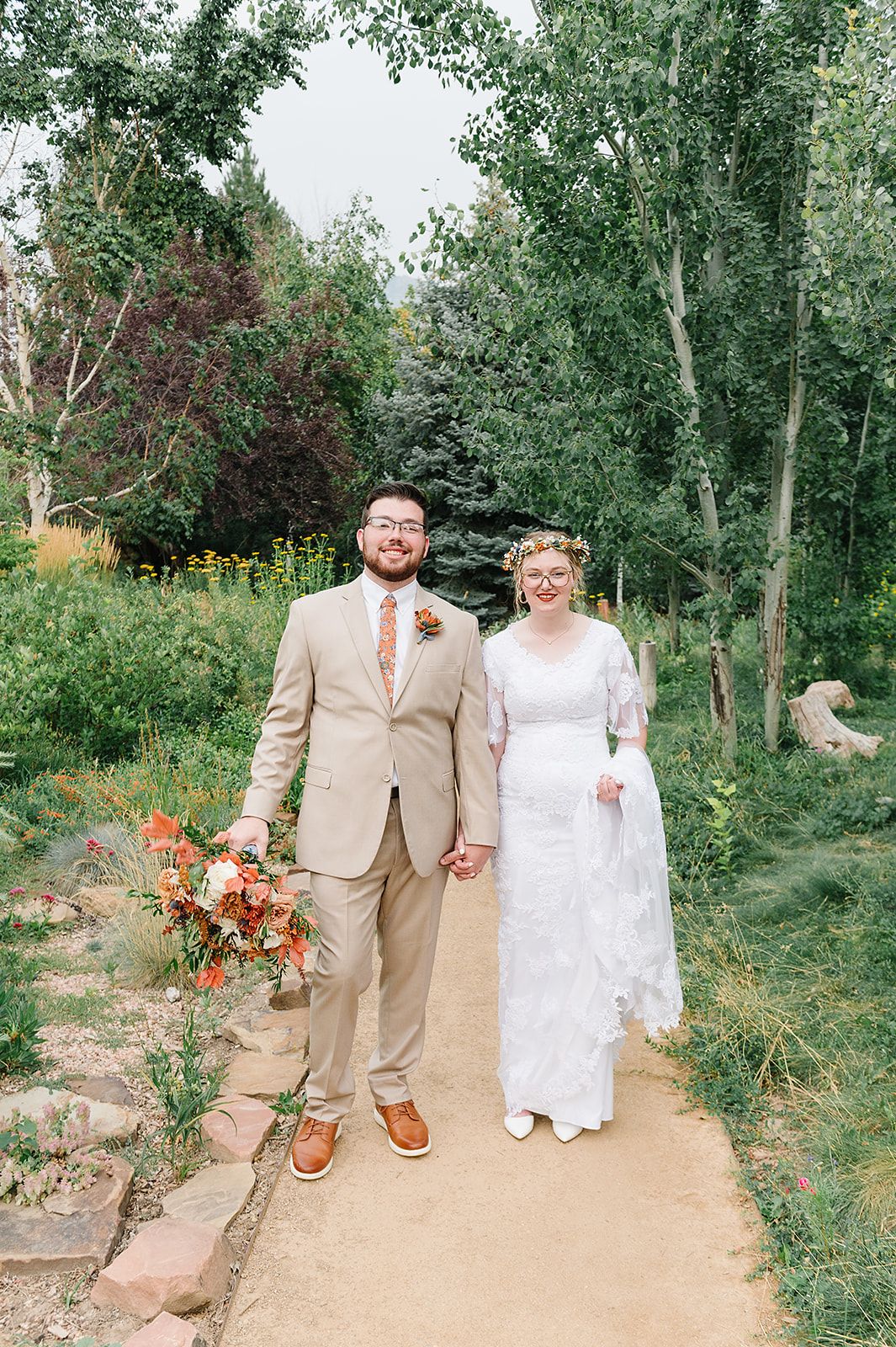 A wedding couple poses on a garden path surrounded by vibrant summer foliage and flowers.