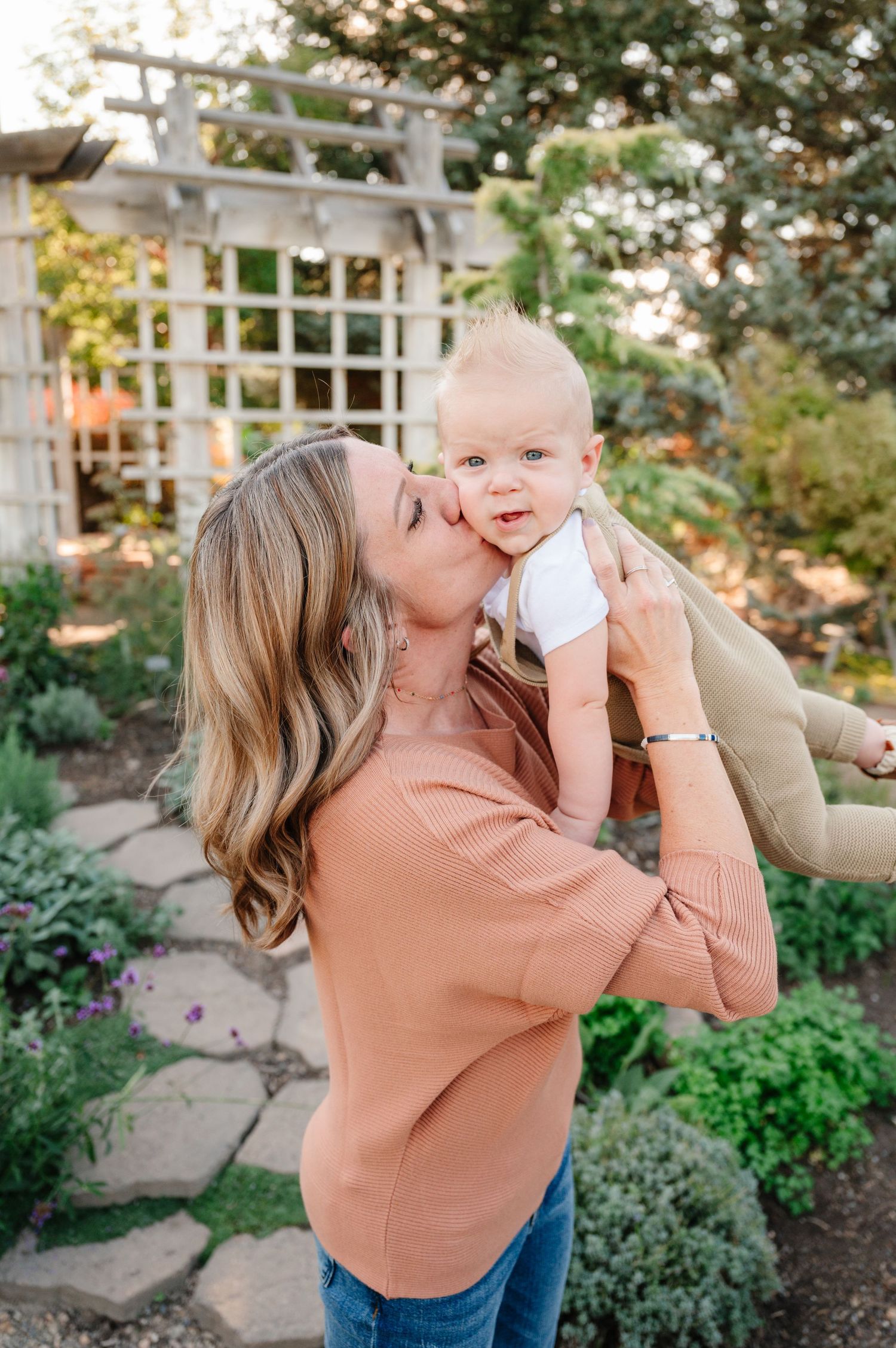 A tender moment between parent and baby in a garden setting with a white pergola.