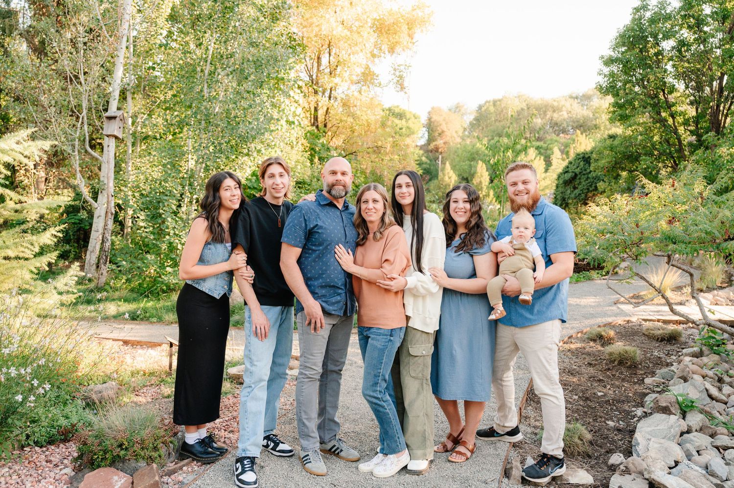 A group poses together on a garden path surrounded by lush greenery during golden hour.