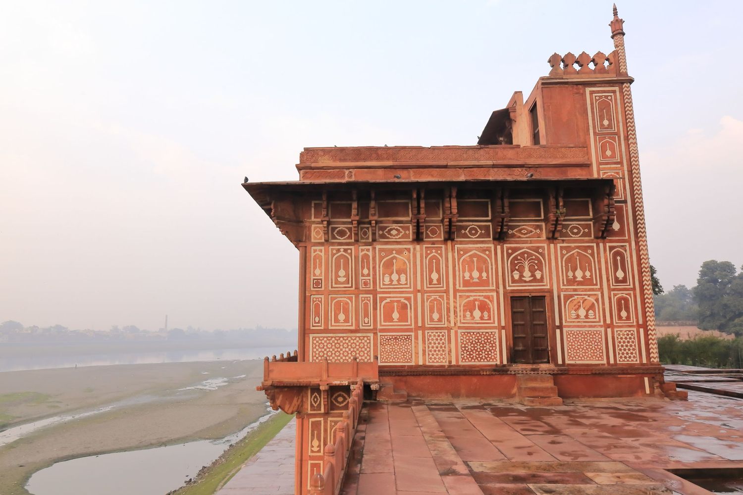 Red sandstone architectural structure with detailed carvings overlooking a river at sunset.