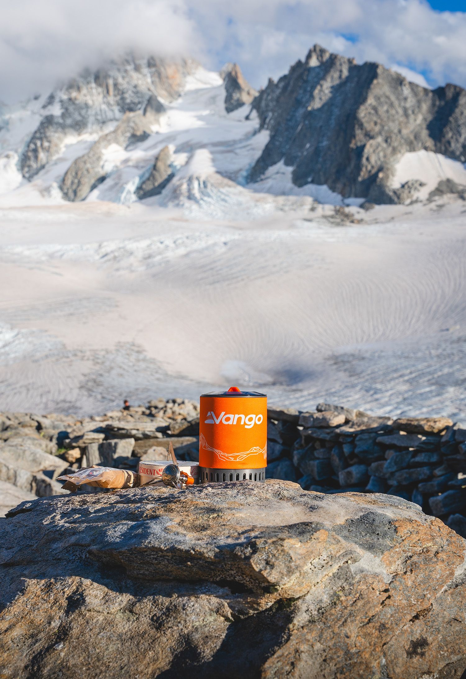 Orange camping stove against dramatic snow-capped mountain backdrop.