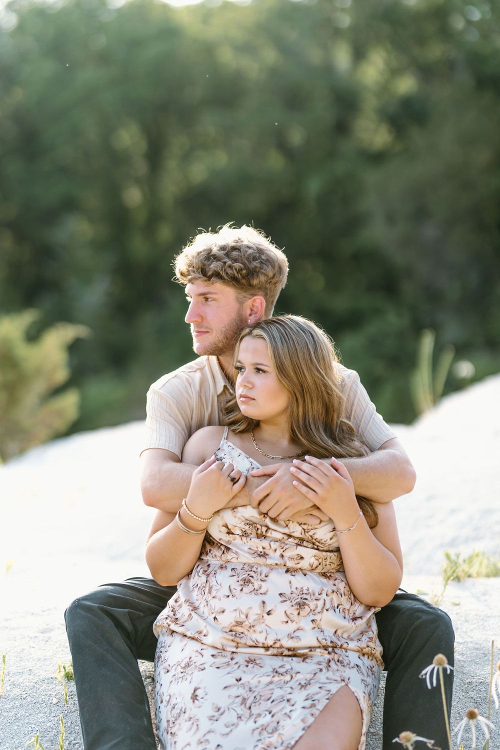 couple sitting with the boy behind girl. he has his arms wrapped around her shoulders and she is holding his wrist.