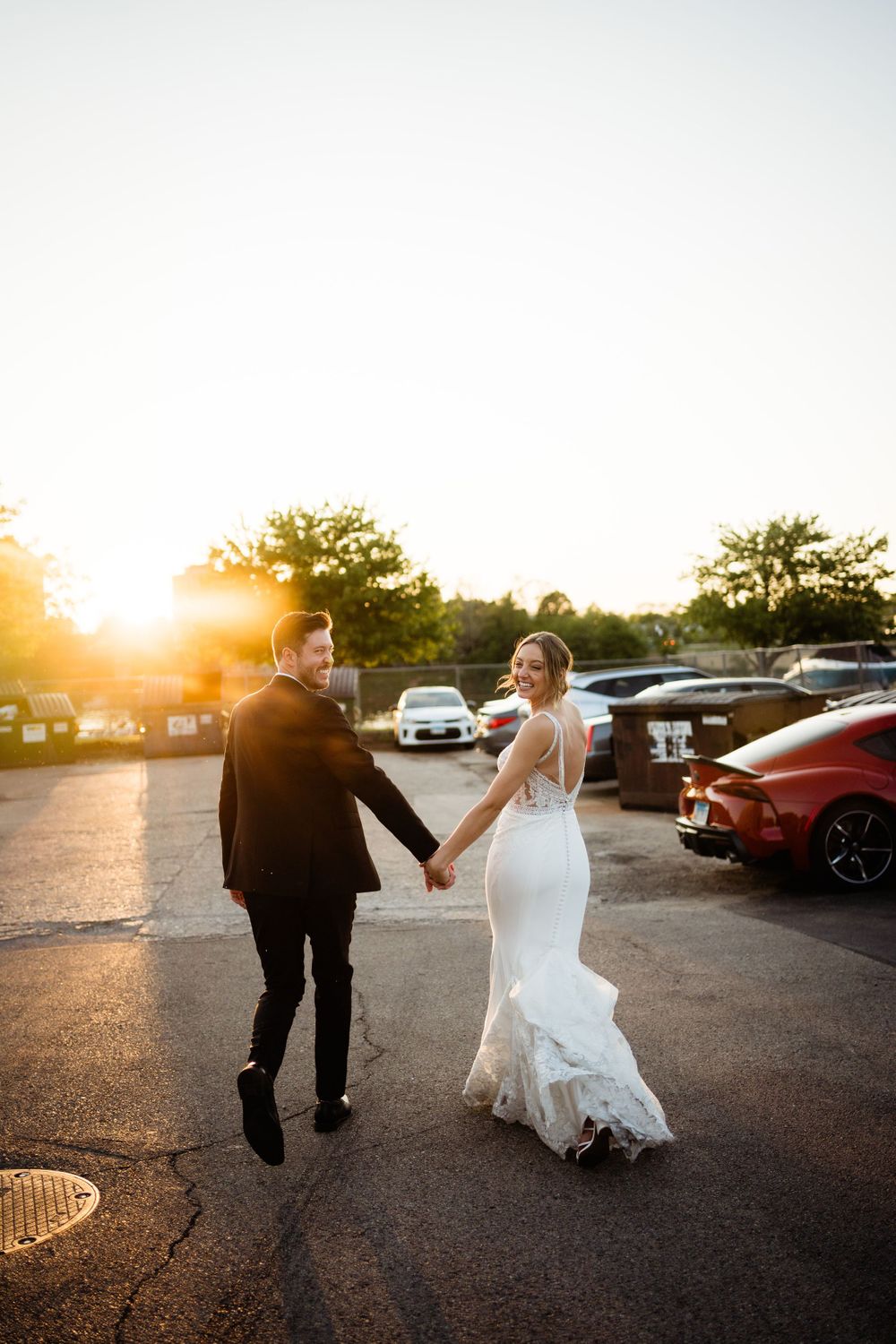 Couple walking hand in hand through parking lot at sunset after wedding ceremony.