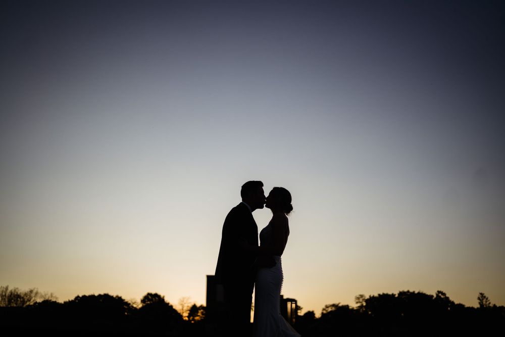 Silhouette of couple kissing against sunset sky during wedding portraits.
