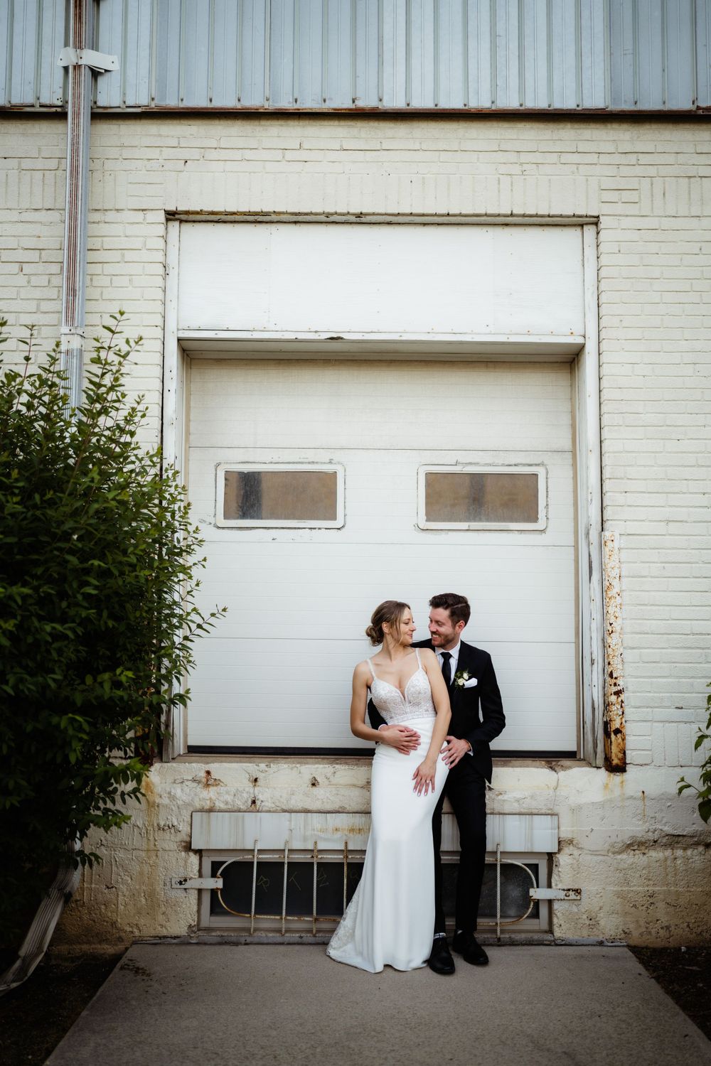 Couple posing against industrial white garage door for wedding portraits.