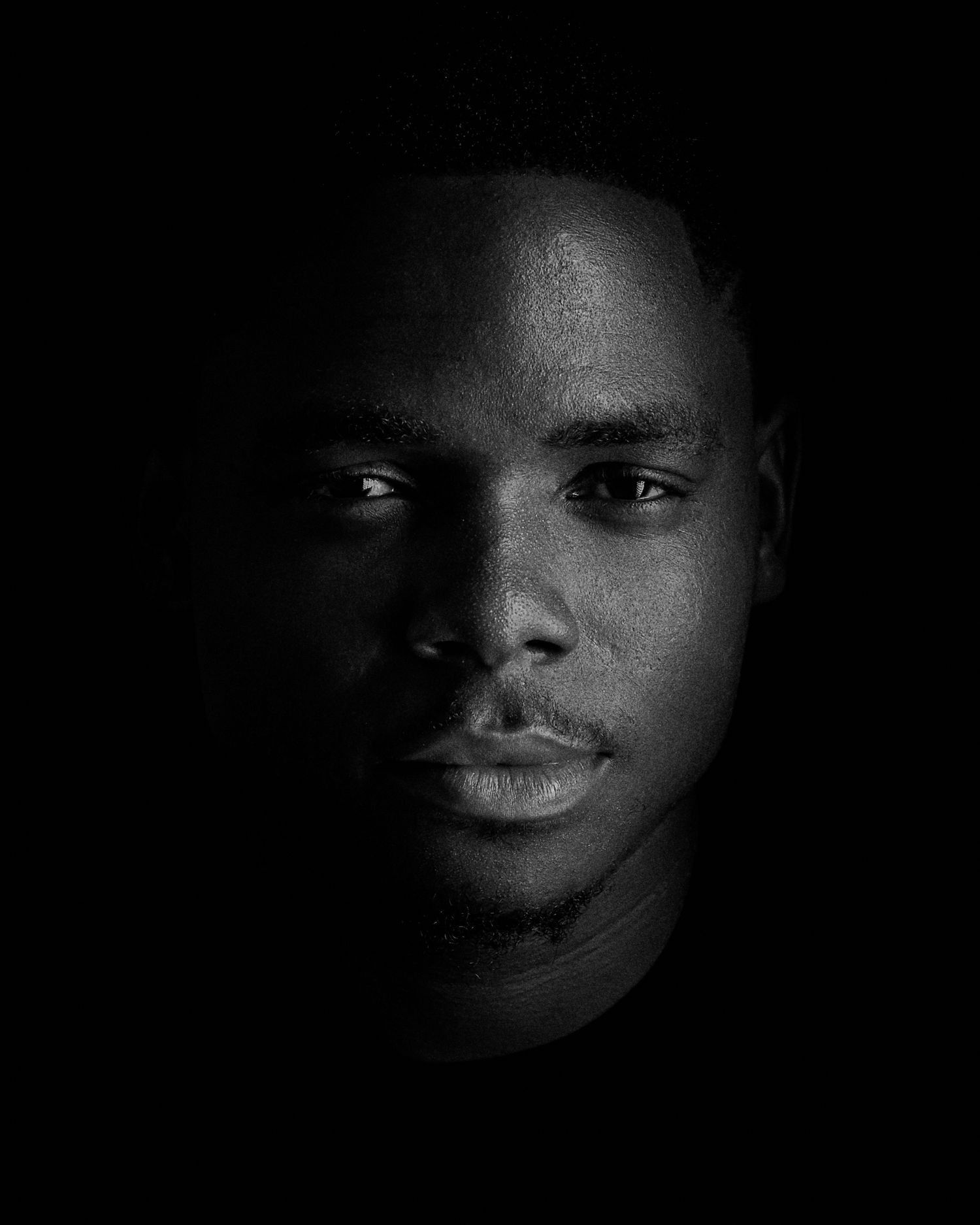 Dramatic black and white portrait with dramatic side lighting against dark background.