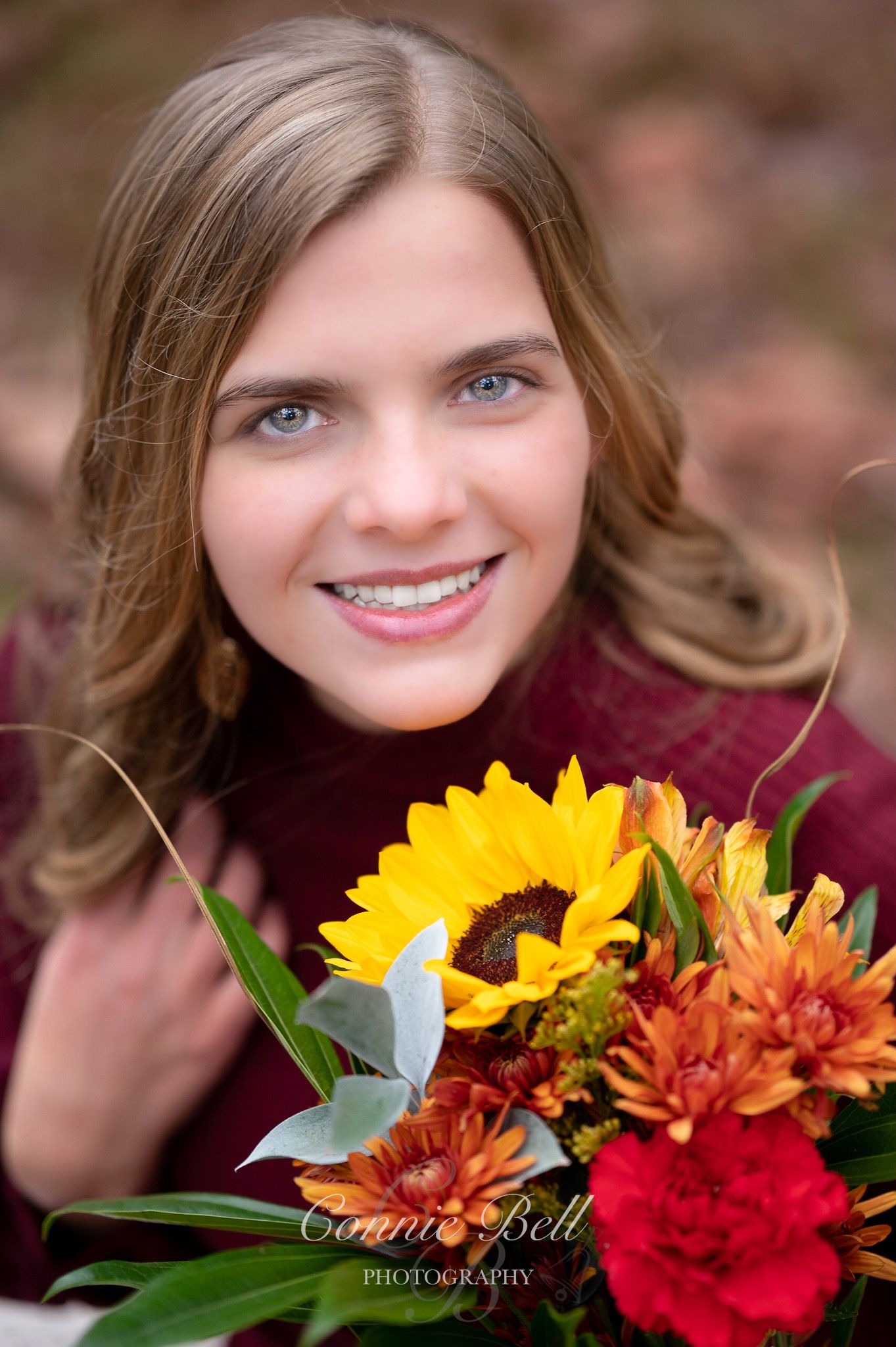 Autumn portrait with burgundy sweater holding vibrant sunflowers and fall flowers.