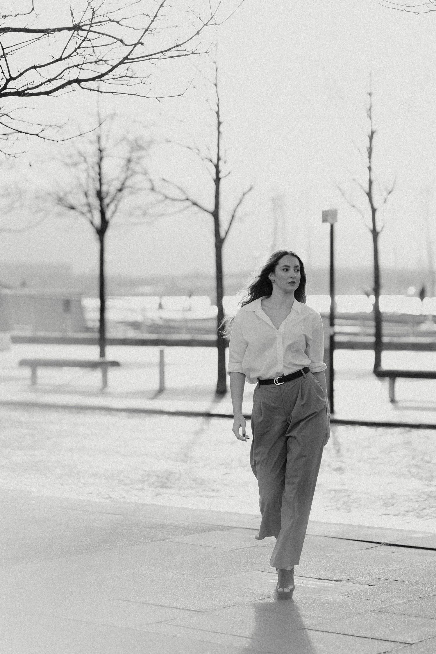 Person in loose clothing runs through winter landscape with bare trees.