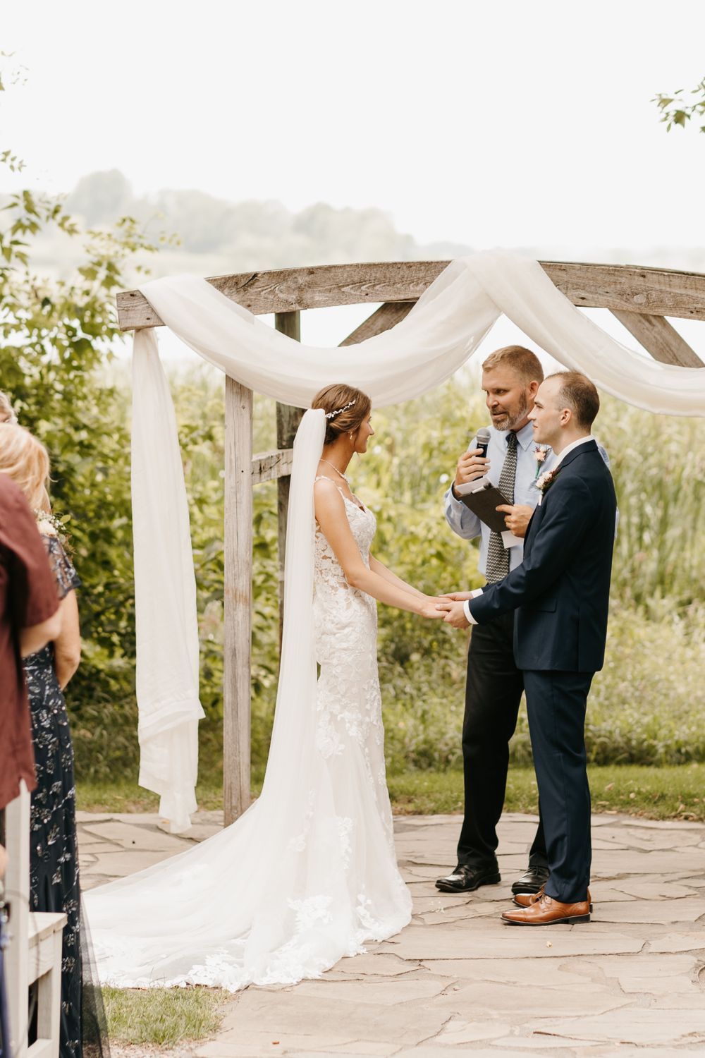 Bride and groom hold hands during outdoor wedding ceremony at rustic wooden altar.