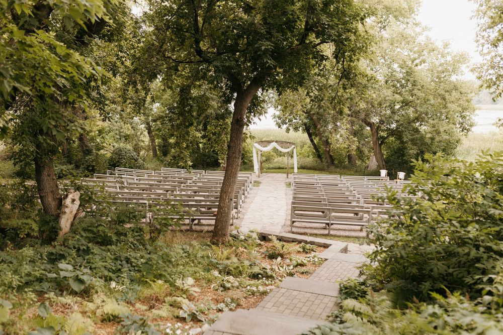 Elegant outdoor wedding ceremony setup with white chairs and floral arch in a lush green garden.